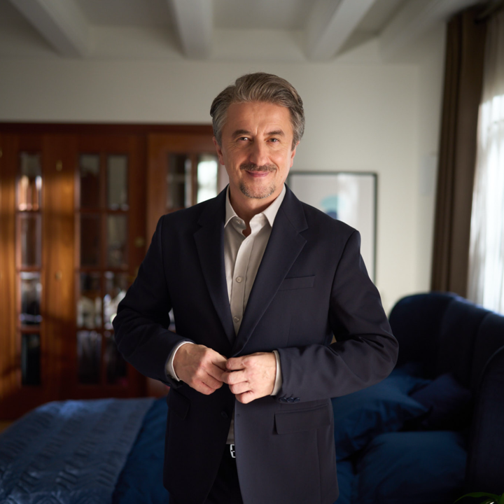 Older man with greying hair and a moustache in a dark blue suit and grey shirt