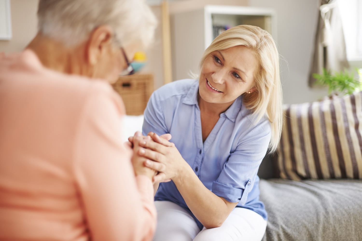 Carer holding an older woman's hands while providing support at home
