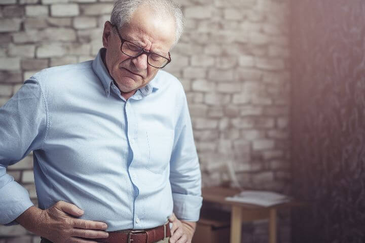 elderly man holds his stomach from constipation